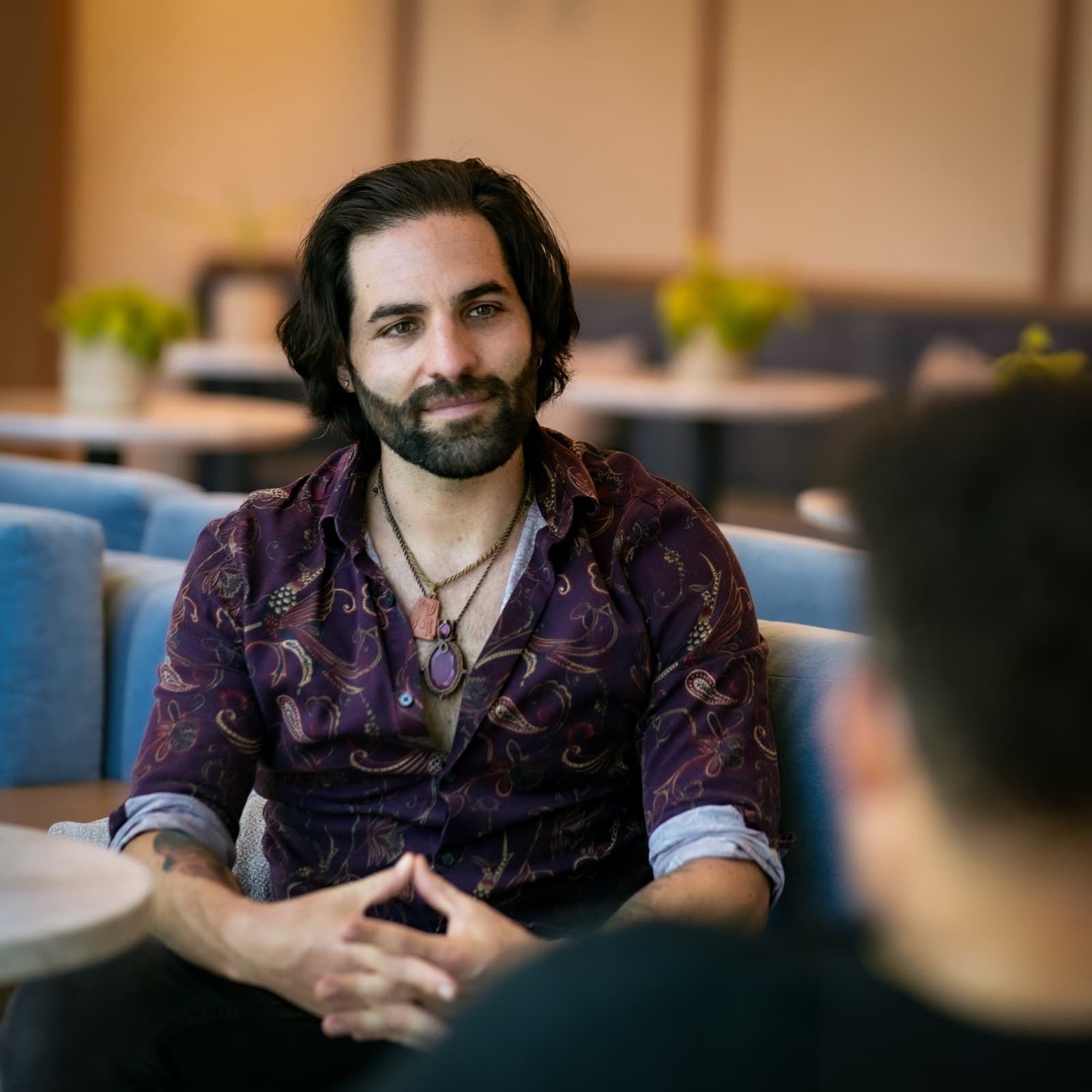 Joseph Buchoff in a session, seated in a plum paisley shirt with his hands steepled, listening to a client